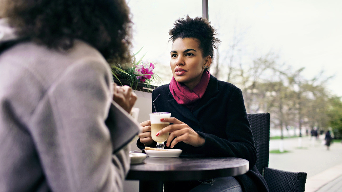 Two women have coffee at an outdoor cafe