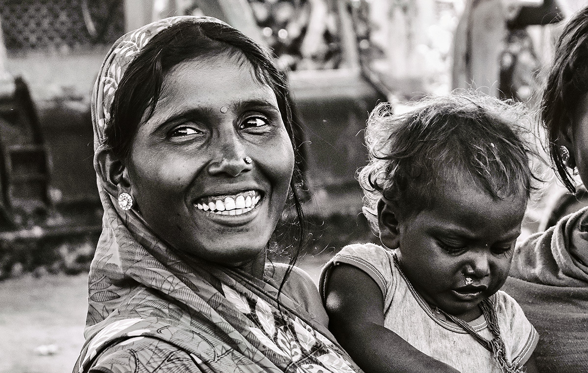 Indian woman wearing sari sits holding baby while turning toward camera and smiling broadly.