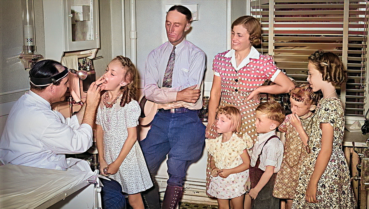 Old-time doctor sees family in his office - family is father, mother daughters and sons.