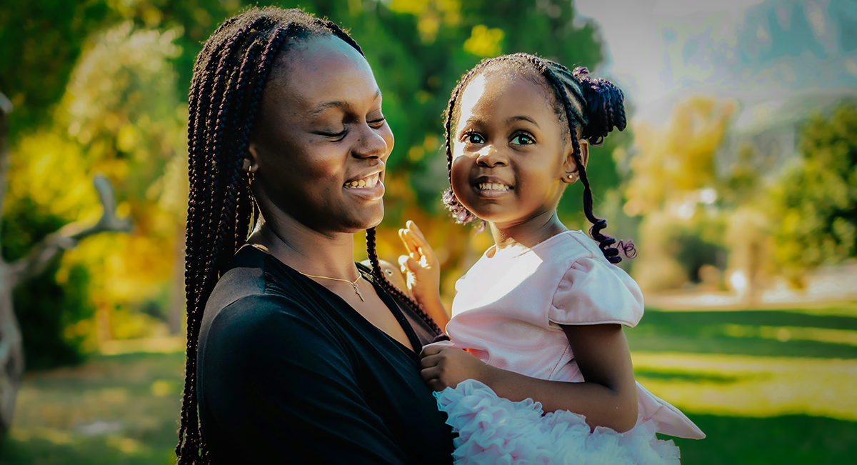 Smiling black mom holds beautiful infant daughter in pink dress.