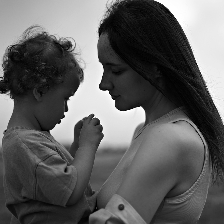 Mother and infant child in silhouette, mother on the right, in pensive quiet intimate mood.